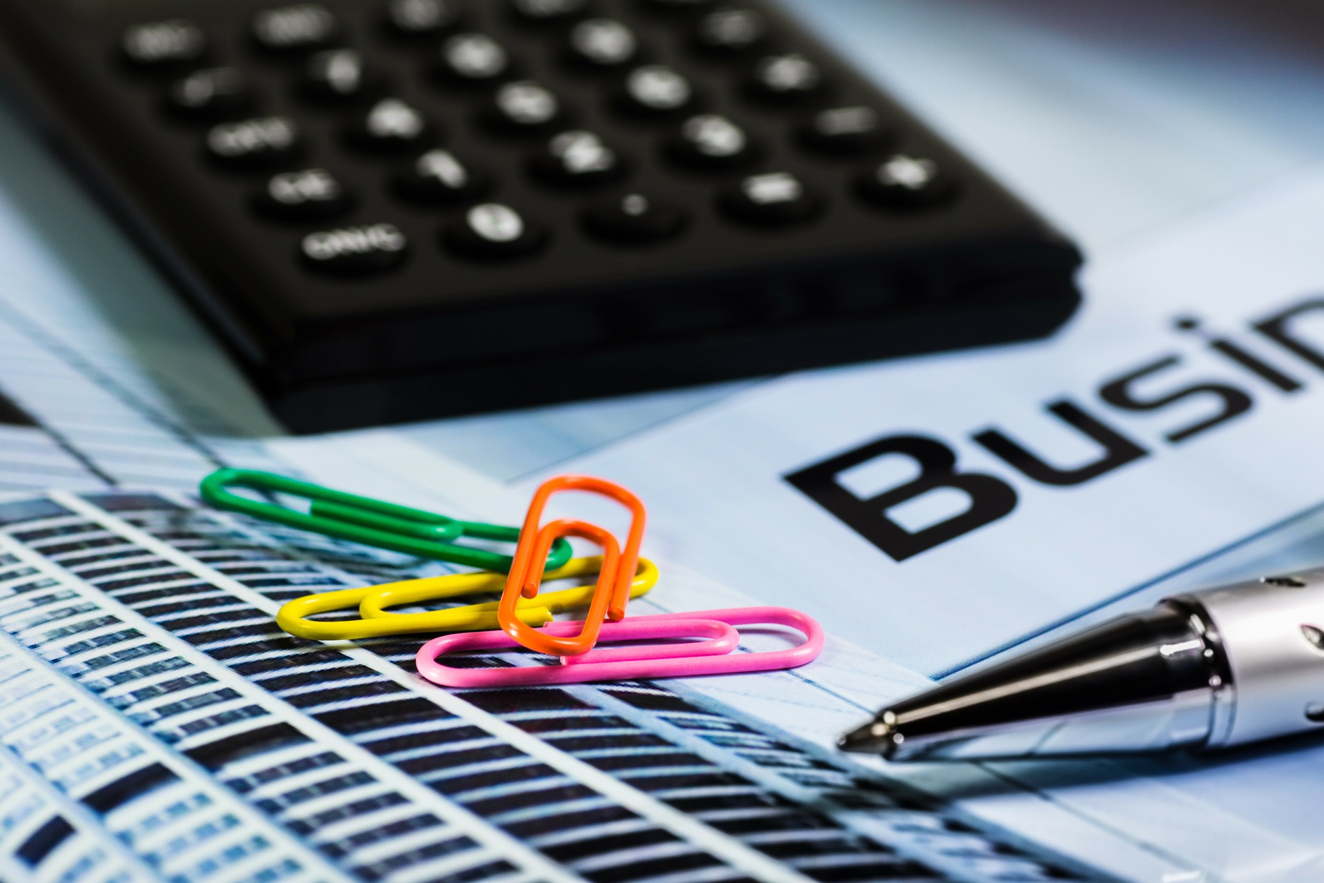 Photo of a pile of colorful paperclips sitting on business forms with a calculator and pen.