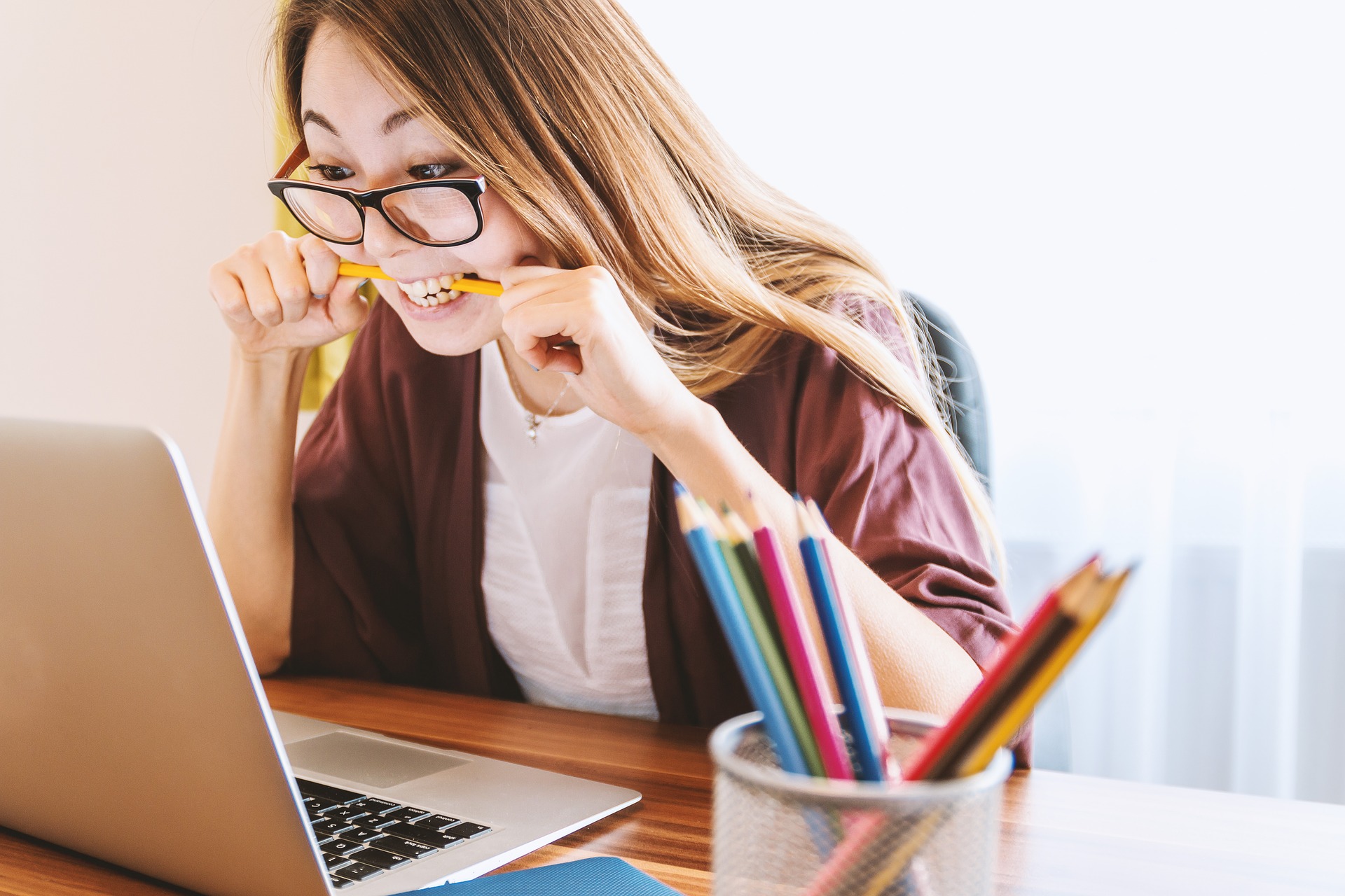 Photo of a distressed woman biting a pencil while looking at a computer.