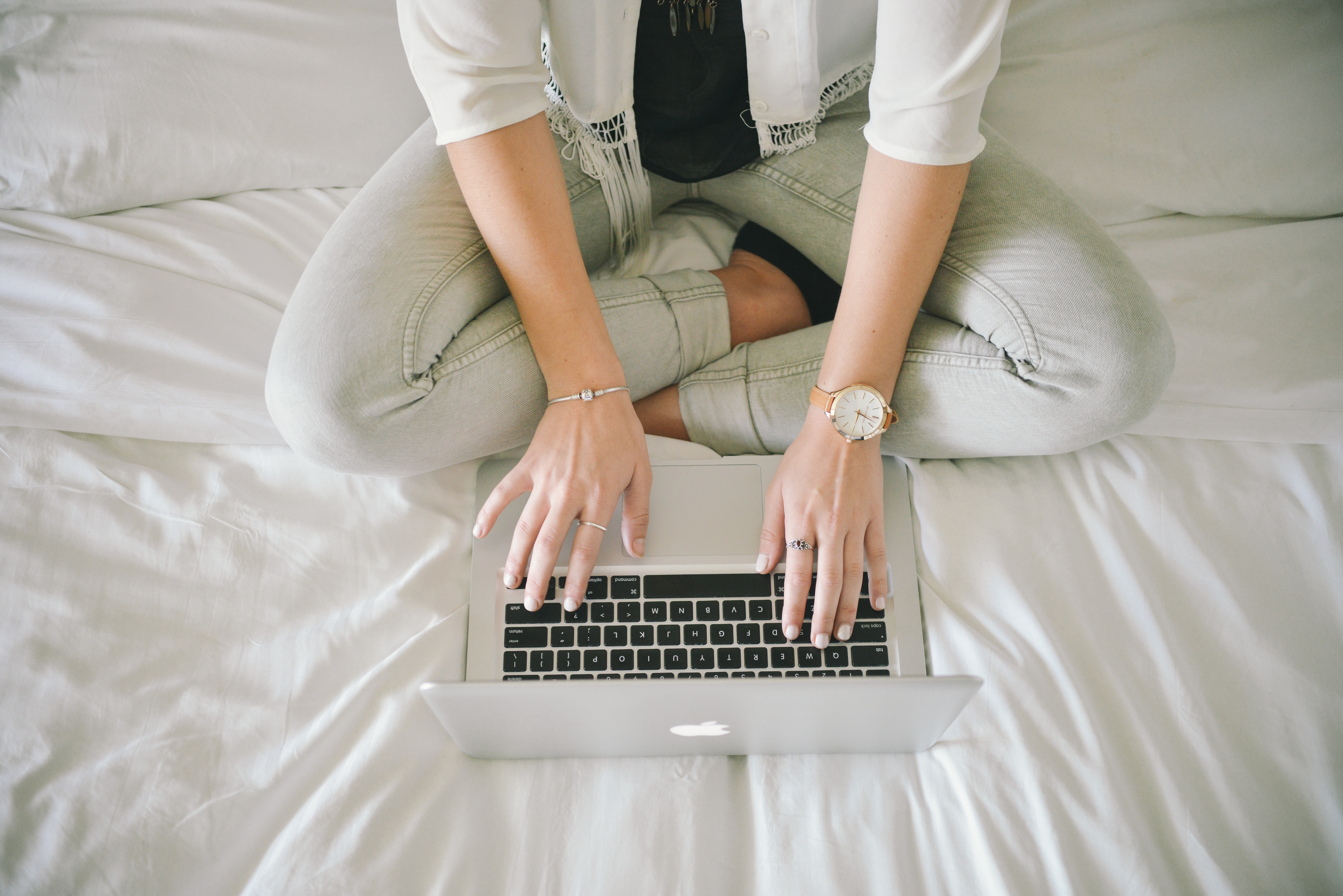 Photo of a woman sitting on a bed writing on a laptop.