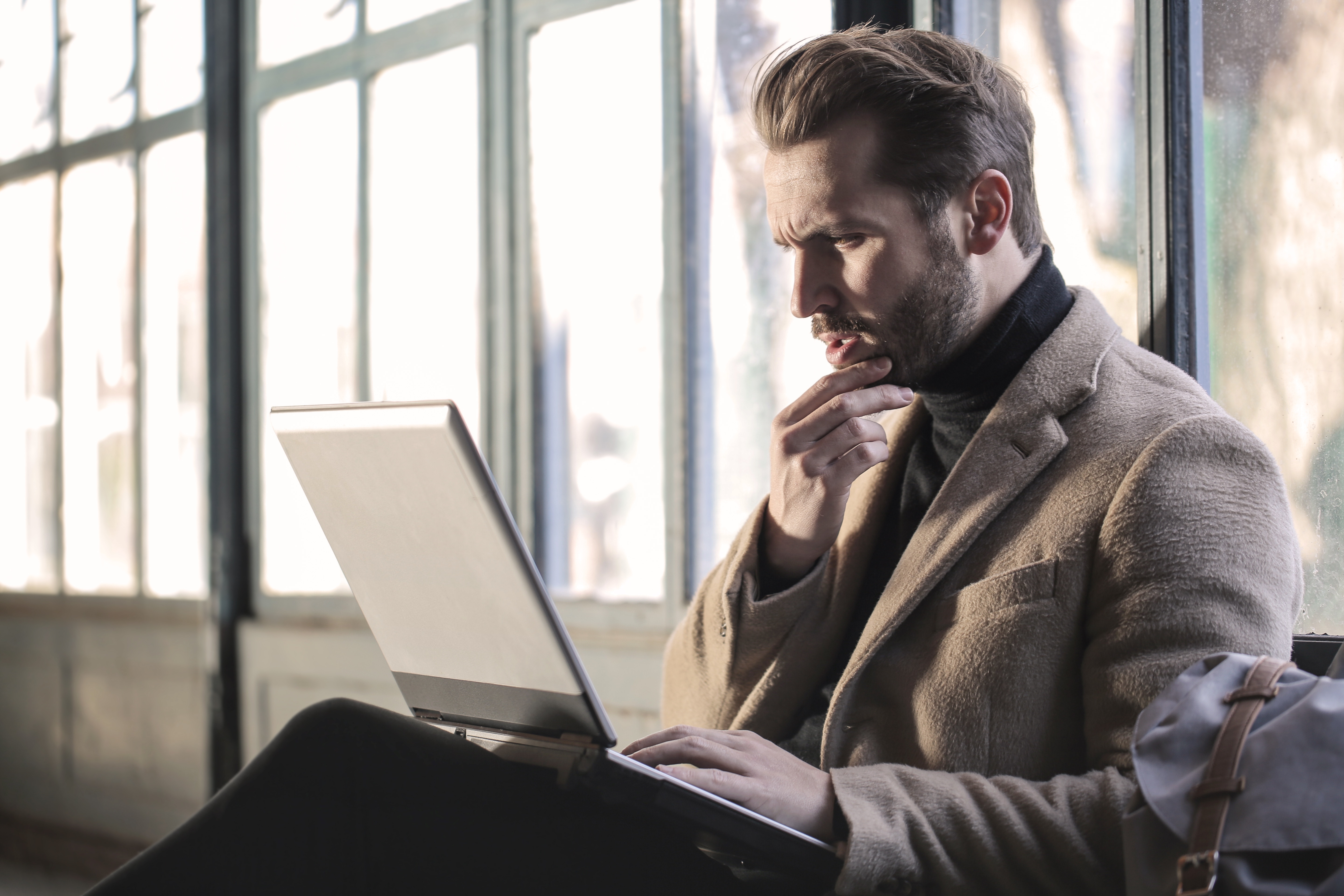 Freelance writer sitting on the floor, frowning at his laptop computer.