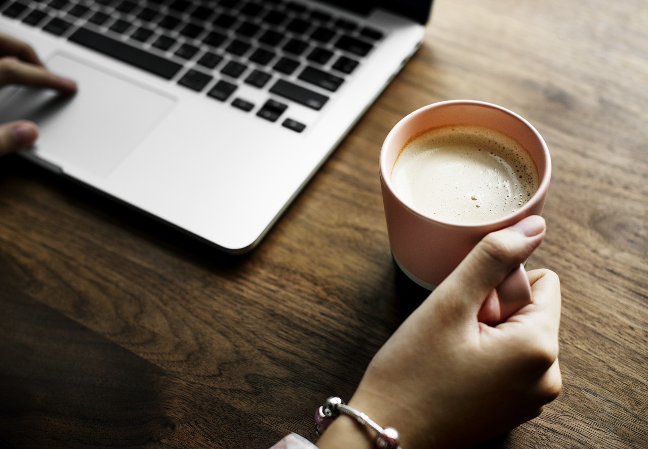 Photo of a woman browsing on her laptop while drinking coffee.