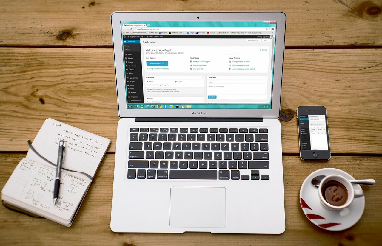 Photo of a laptop with a notebook and coffee cup nearby.