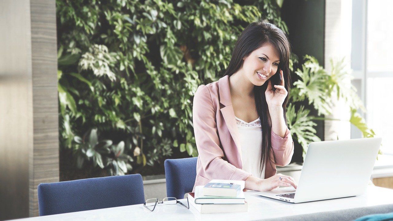 Photo of a woman talking on the phone while using her laptop.