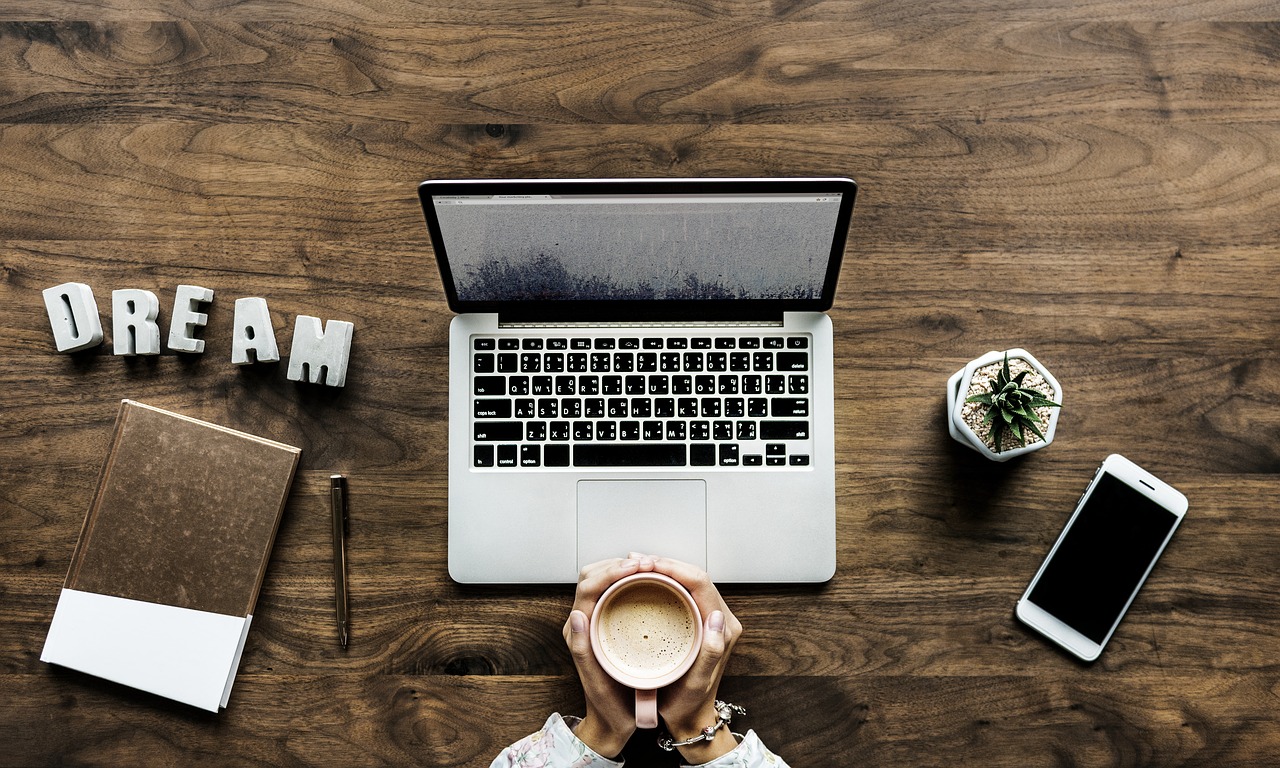 Photo of a woman holding a cup of coffee in front of laptop.