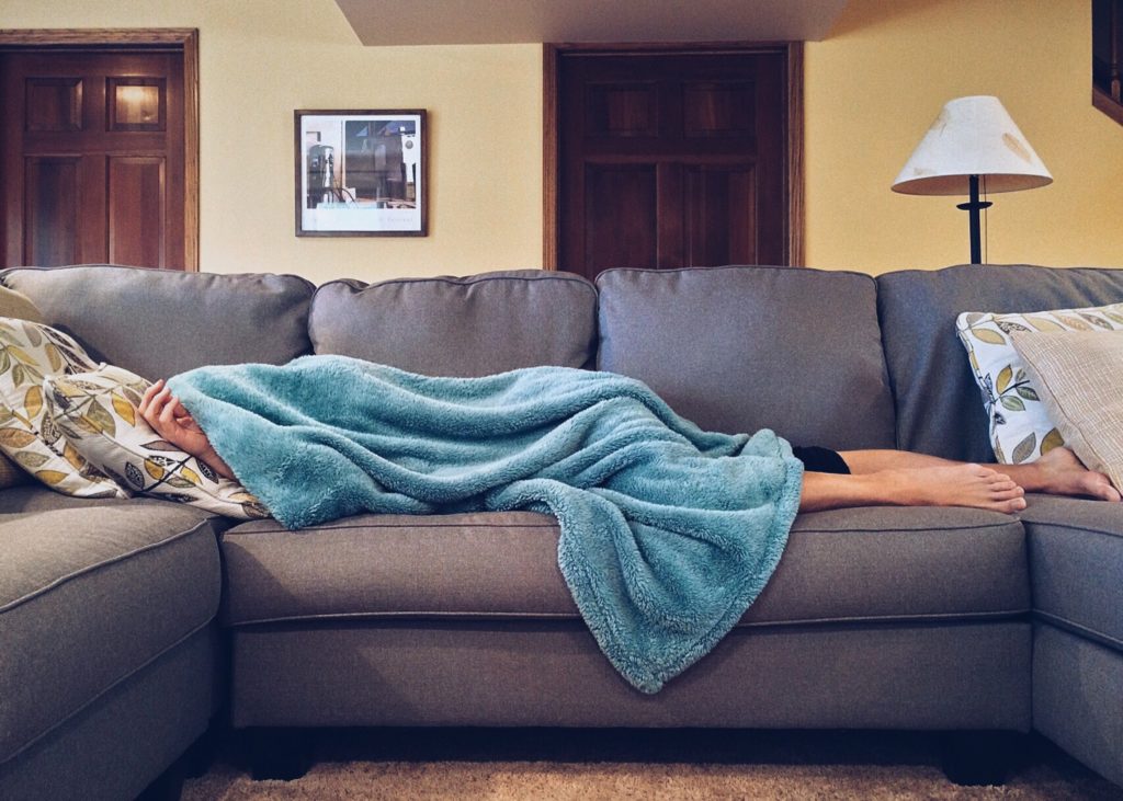 Photo of a person sleeping beneath a blanket on a couch.