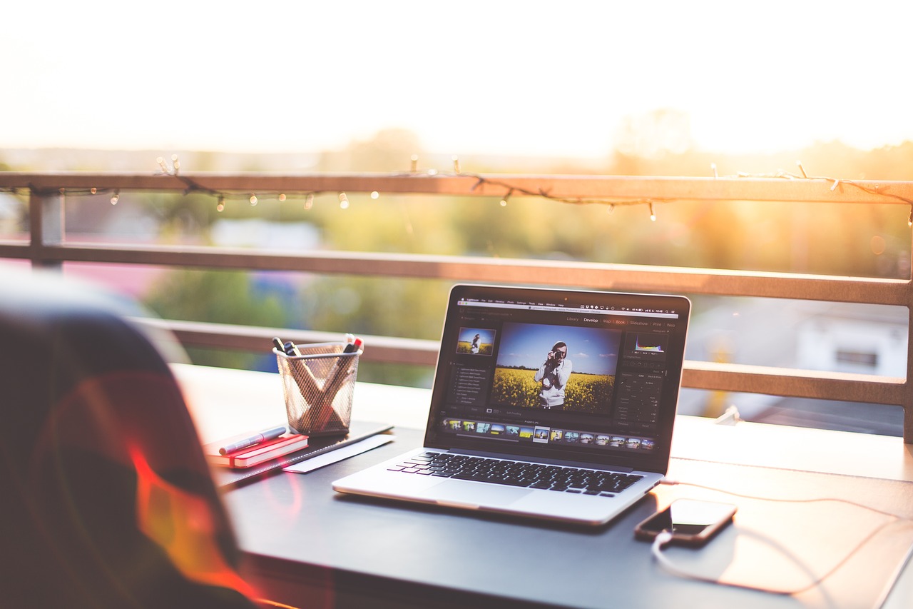 Photo of a laptop on a desk outside, with lights on the railing.