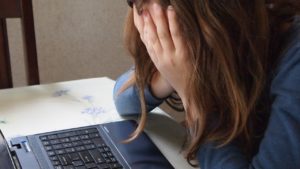 Photo of a laptop and an upset woman with her head in her hands.