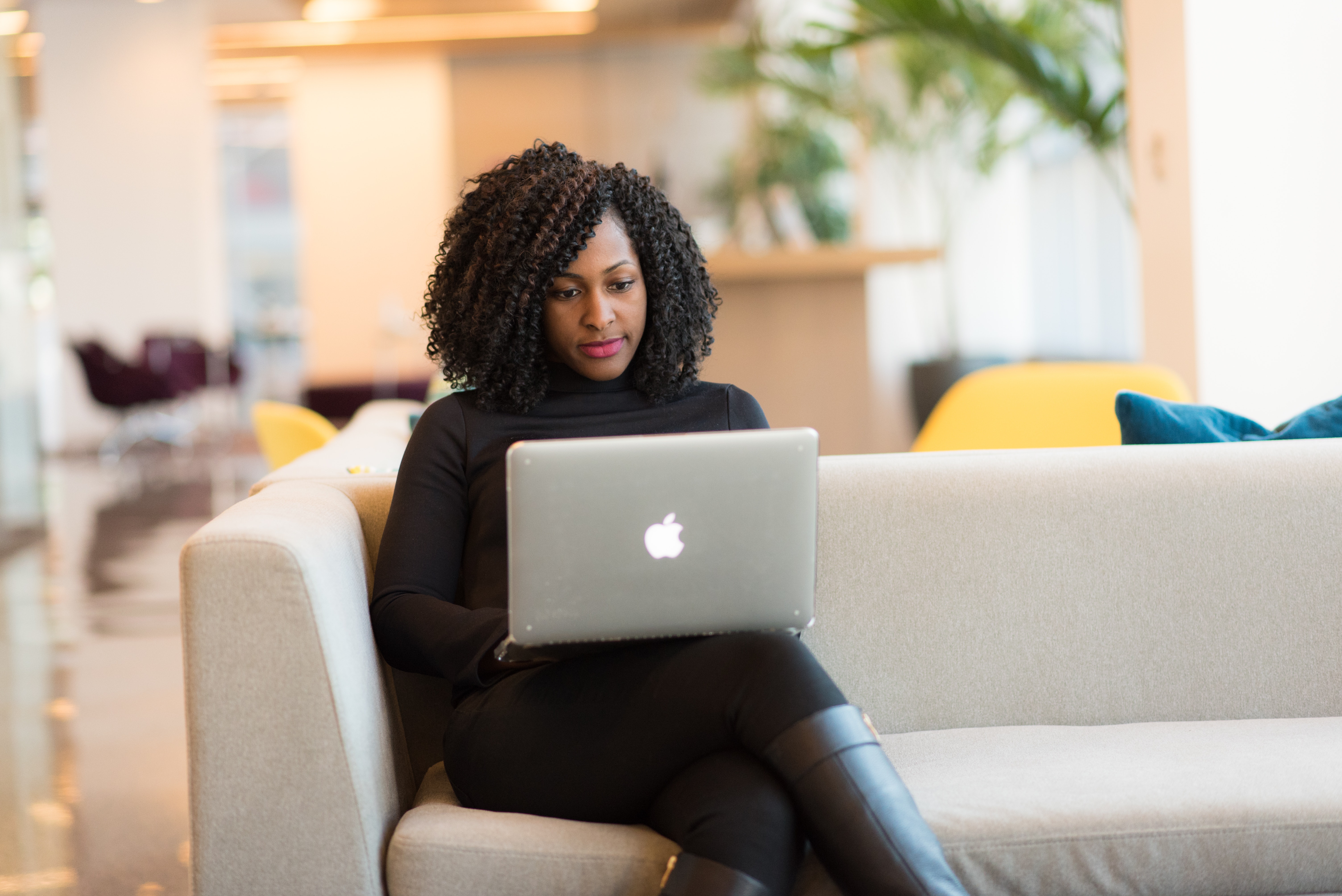 Photo of a woman working on a laptop while sitting on a sofa.