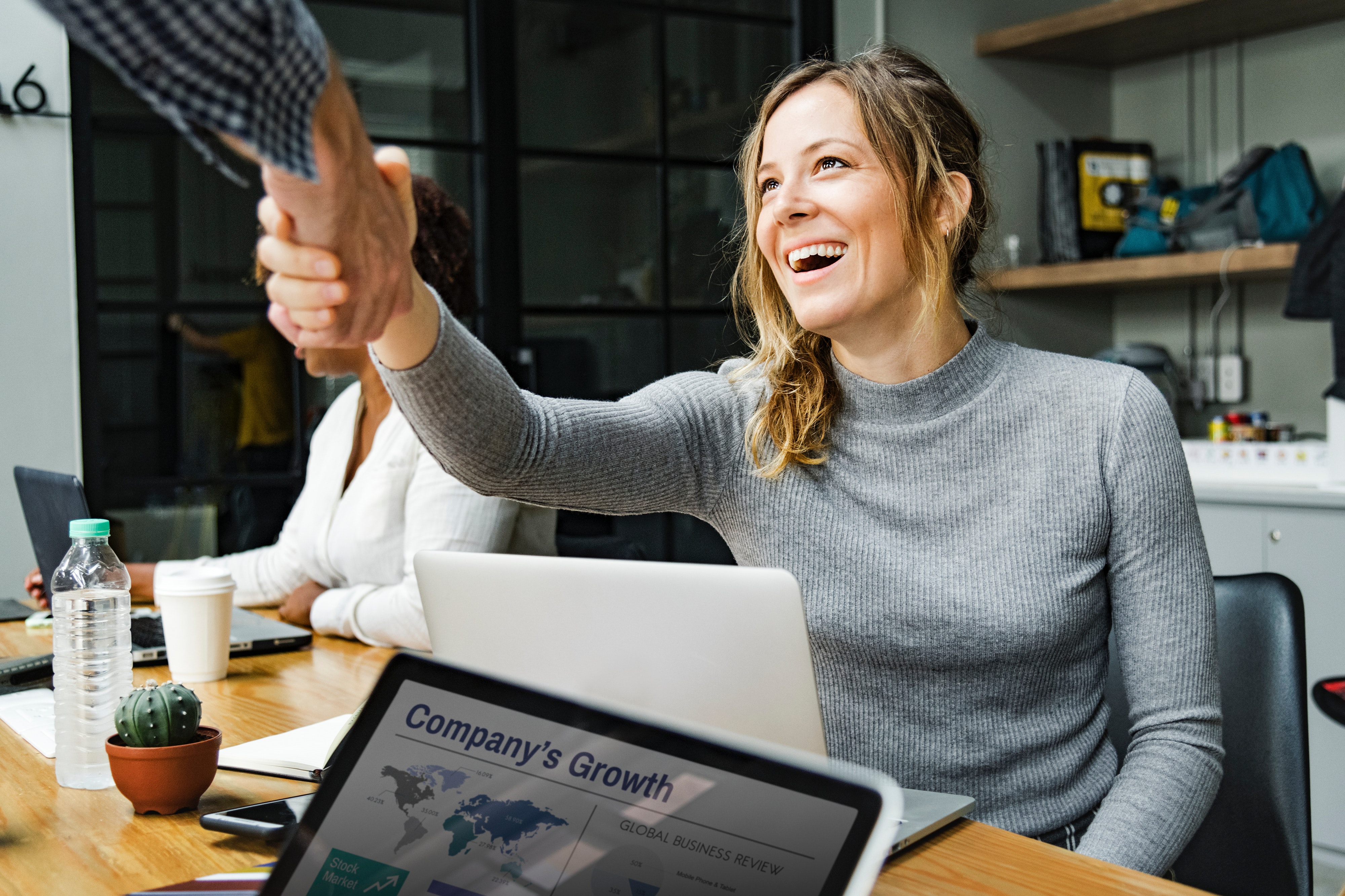 Photo of a woman with a laptop shaking a man's hand.