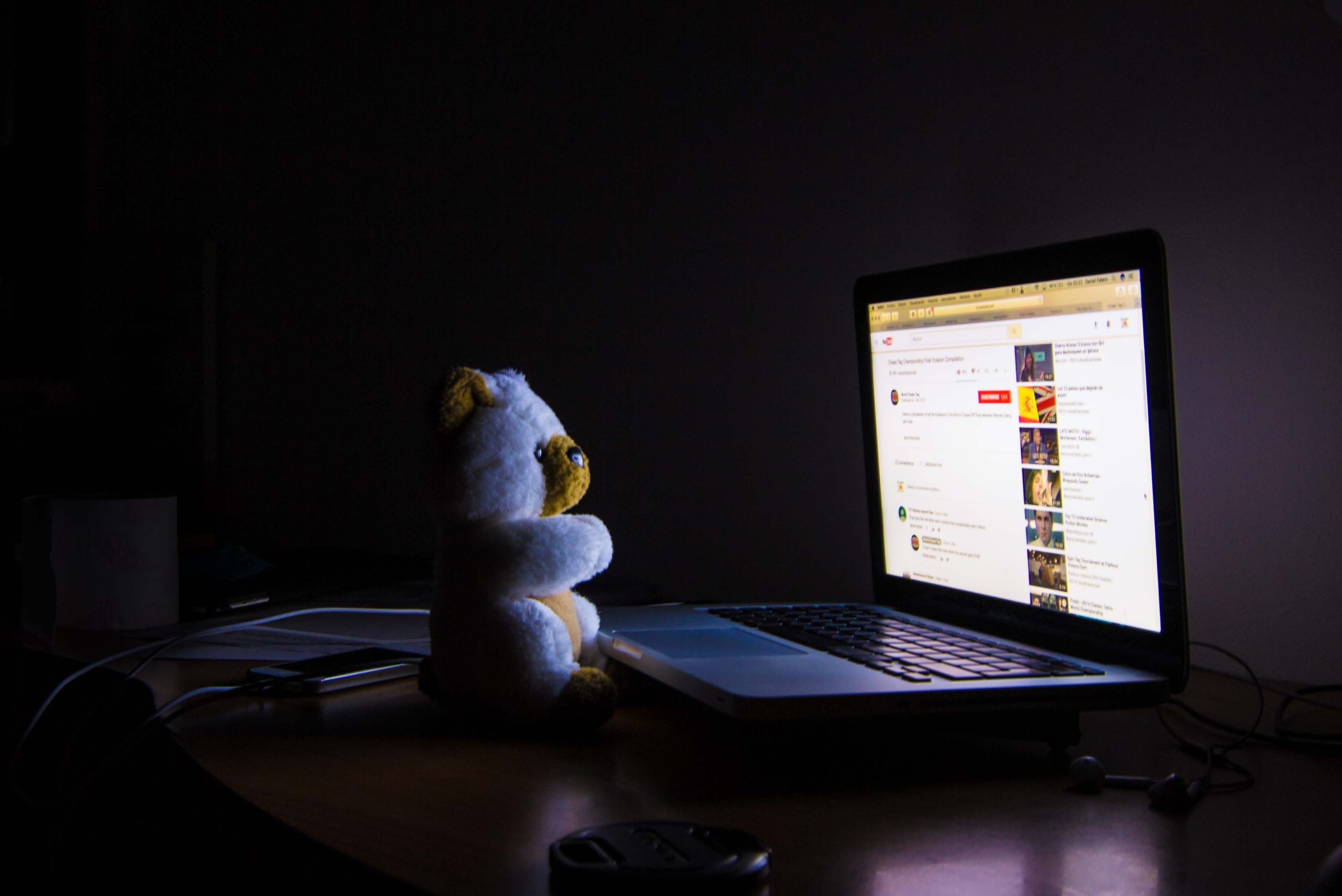 Photo of a laptop in a dark room with a teddy bear.