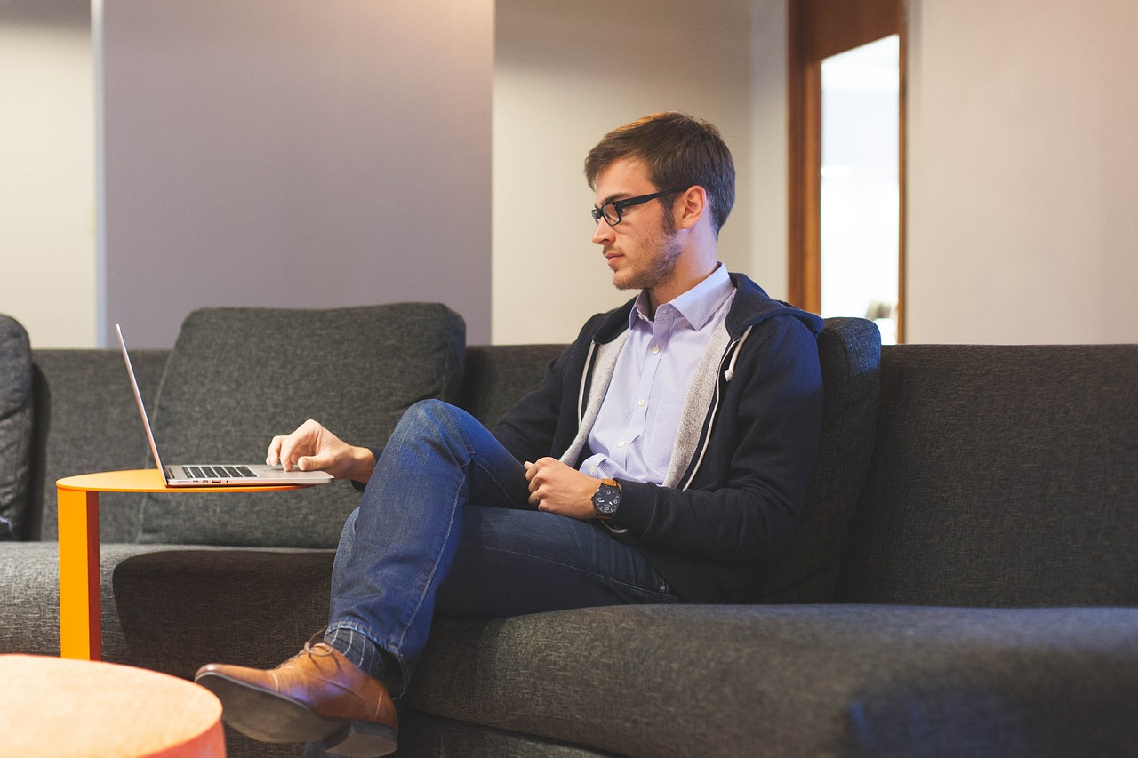 Photo of a young business owner sitting on a couch and working on a laptop.