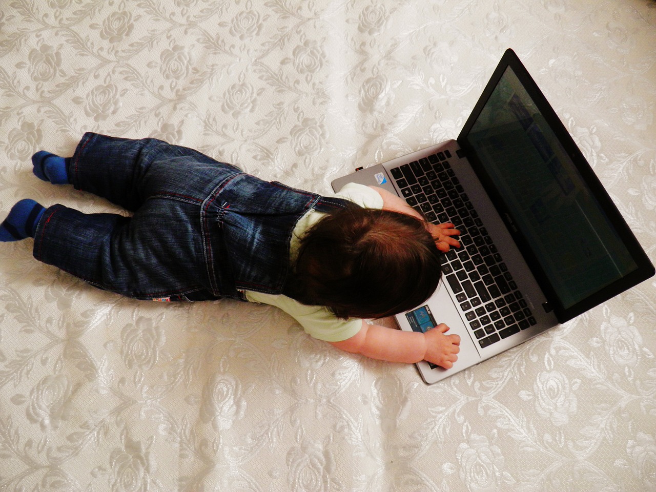 Photo of a baby lying on a bed with a laptop computer.