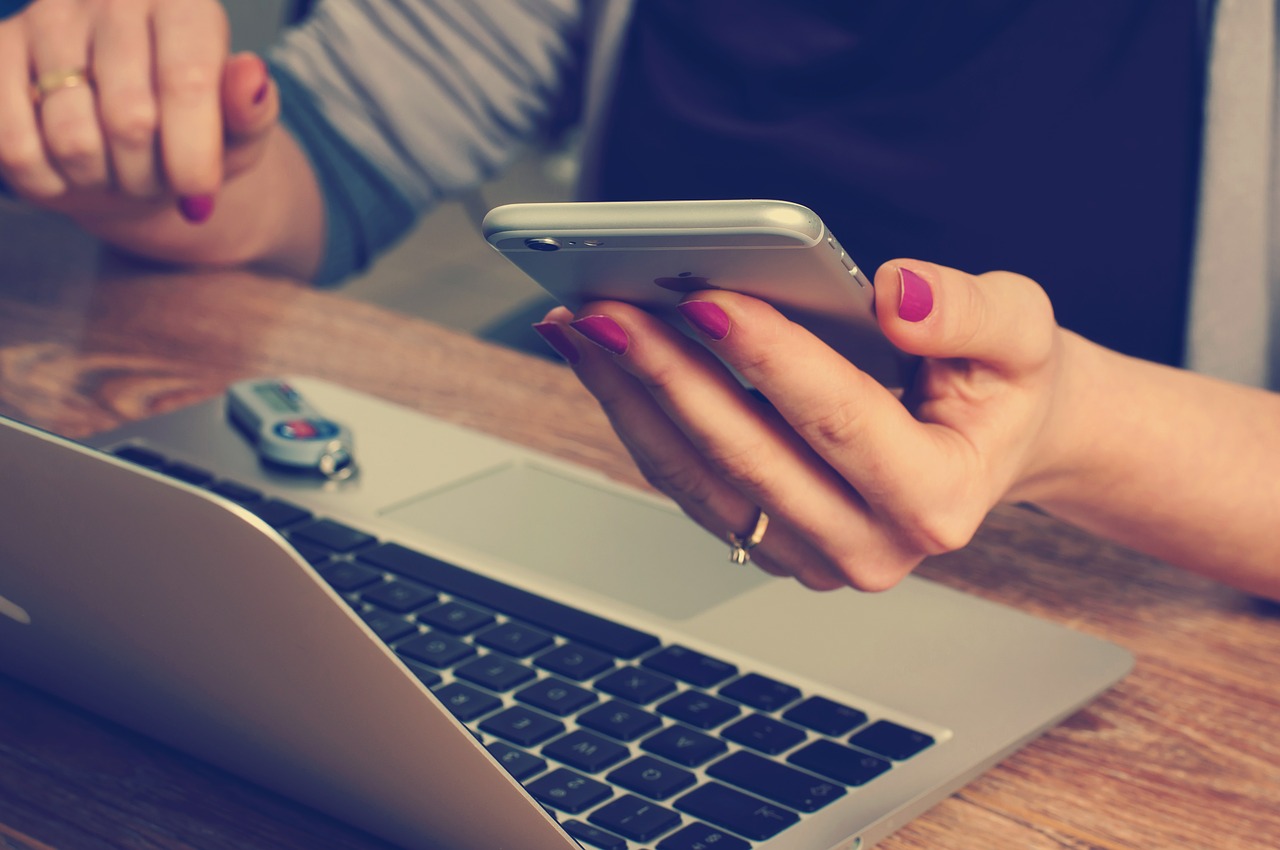 Photo of a woman holding a smartphone in front of a laptop.