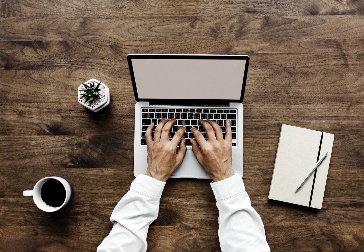 Photo of a man working on a laptop at a wooden desk.