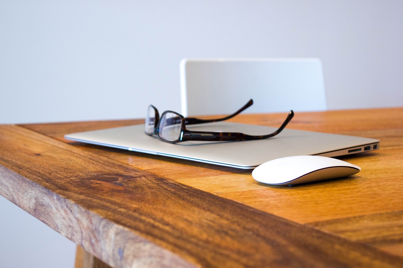 Photo of a closed laptop on a desk with glasses and a mouse.