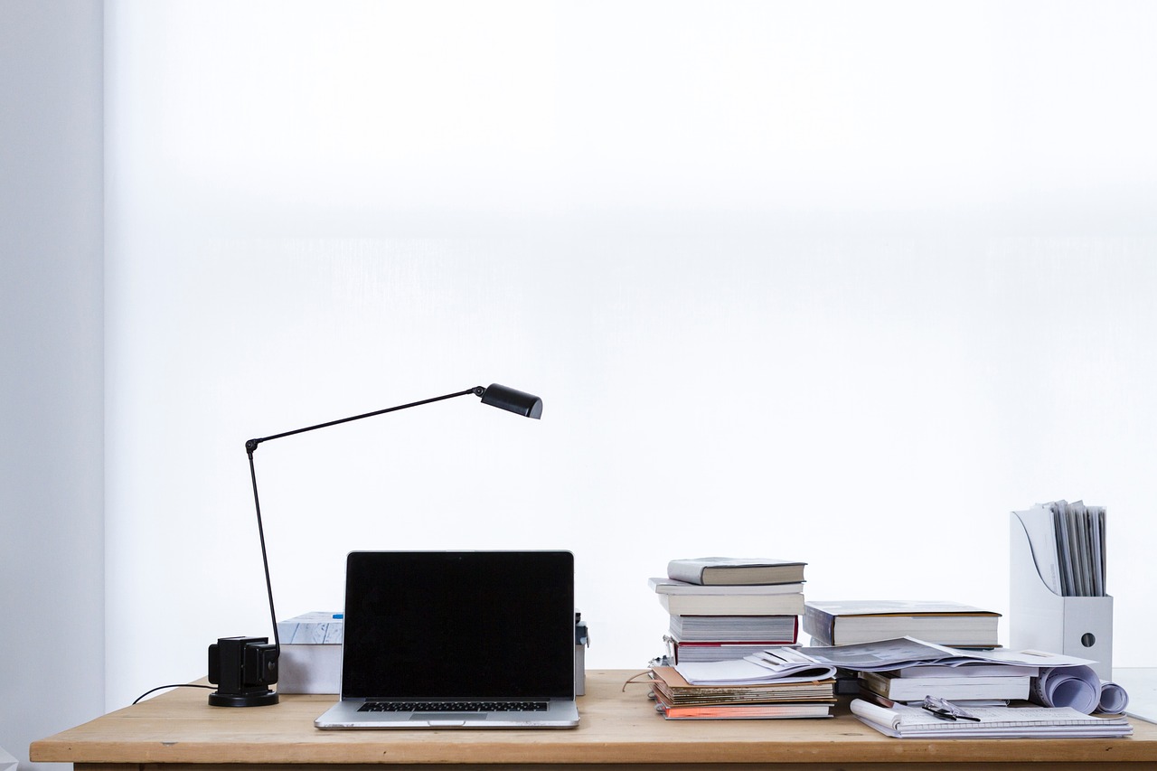 Freelance writer's laptop on a desk with a pile of books.